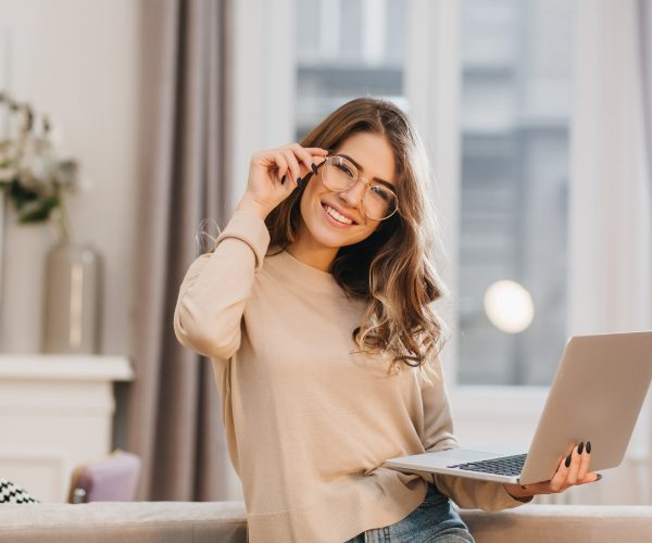 cute-girl-in-beige-shirt-touching-glasses-and-holding-laptop-with-smile